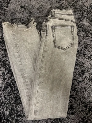 Grå jeans low bootcut från 157 - Snygga grå jeans från 157 med low bootcut-modell. Jeansen har en klassisk femficksdesign och råa, fransiga benslut för en trendig look. Tillverkade i denim med en ljusgrå tvätt och svarta sömmar som ger extra edge. Är lite tramsiga vid slutet av benen pågrund av att dem har varit för långa på mig