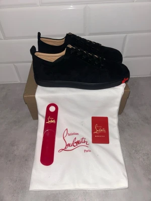 Svarta sneakers Christian Louboutin - Snygga svarta sneakers Christian Louboutin i mocka med klassisk låg siluett. Skorna har svarta skosnören, diskret logga och den ikoniska röda detaljen framtill på sulan. Kommer med påse, skohorn och kort.