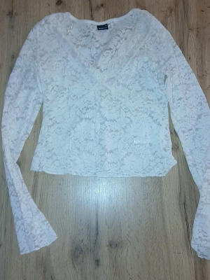 Vit spetsblus med v-ringning - Säljer en vit, långärmad blus från Bik Bok i genombruten spets med v-ringning. Blusen är croppad och har ett romantiskt blommönster i spetsen. Perfekt för dig som gillar en feminin och trendig stil.