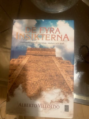De fyra insikterna - En spirituell bok av Alberto Villoldo som utforskar jordbeskyddarnas uråldriga visdom, insikter och kraft. Omslaget har en bild av en mäktig stenpyramid mot en blå himmel med moln. Perfekt för dig som gillar andlighet och personlig utveckling.
