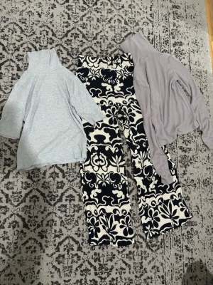 Två polotröjor i olika färger och en byxa  - Säljer två polotröjor, en i ljusgrått och en i ljuslila. Båda har lång ärm och hög krage, perfekta för lager på lager och en clean look. Passar till både jeans och mönstrade byxor för en trendig outfit.