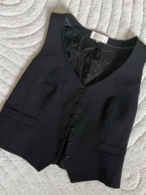 Svart väst  - Stilren svart väst med djup v-ringning. Västen är ärmlös.