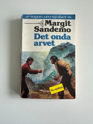 Bok ”Det onda arvet” av Margit Sandemo - Säljer boken 'Det onda arvet' av Margit Sandemo, del av serien Sagan om Isfolket. Omslaget har illustrationer med dramatiska scener i bergsmiljö och vinterlandskap. Boken är i pocketformat med färger i blått, vitt och brunt. Perfekt för dig som gillar spänning och fantasy.