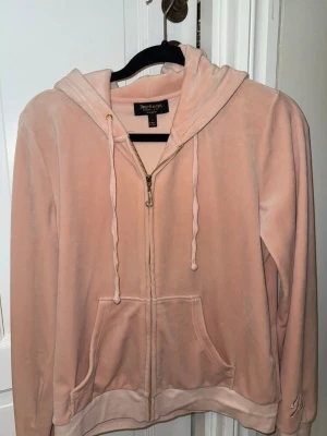 Ljusrosa velour hoodie Juicy Couture - Mjuk och skön ljusrosa hoodie från Juicy Couture i velourmaterial. Dragkedja framtill, två fickor och justerbar huva med snören. Jätte fint J med stenar på (alla är på).Perfekt för en chill och avslappnad stil. Klassisk logga på etiketten i nacken. Har används 1-2 gånger men märks inte.