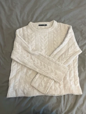 Vit kabelstickad tröja  - Kabelstickad tröja i mjuk, vit ullmix från 157. Tröjan har rund halsringning, långa ärmar och ribbade muddar. Klassisk och enkel design som passar perfekt till jeans eller kjol. Snygg struktur med flätmönster över hela plagget.