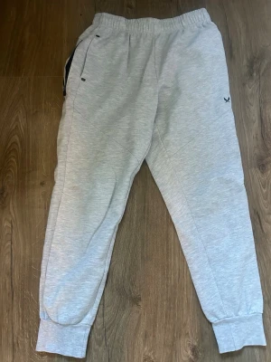 Ljusgrå mjukisbyxor från soc 146-152 - Säljer ett par ljusgrå mjukisbyxor med resår i midjan och muddar vid bensluten. Byxorna har sidofickor och en liten svart logga på vänster lår. Perfekta för chill dagar och gjorda i mjukt material.