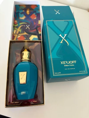 Xerjoff Erba Pura Eau de Parfum 100ml - Lyxig parfym från Xerjoff, Erba Pura, i en elegant turkos flaska med gulddetaljer och matchande exklusiv förpackning. Flaskan har en unik form med guldfärgat lock och etikett. Doften är Eau de Parfum och flaskan rymmer 100 ml.