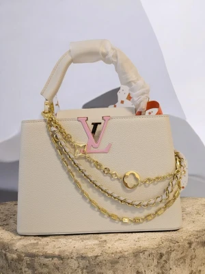 Iouis vuitton Capucines 🤍 - Den här specifika modellen har några utmärkende egenskaper: Design: Den har en sofistikerad benvit färg (off-white) med Iv-logotypen i en ljusrosa ton. Kedja: Den är utrustad med en dekorativ guldkedja i flera lager (multistrand). Modell: Denna storlek kallas vanligtvis Capucines BB eller Capucines MM, vilket är en av Iouis vuittons mest exklusiva och klassiska väskmodeller.
