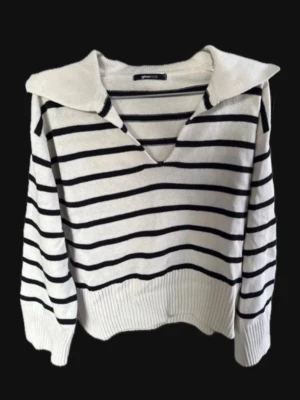 Vit stickad tröja med marinblå ränder - Vit stickad tröja med svarta ränder och bred krage. V-ringad med långa ärmar och ribbstickade muddar. Perfekt för en skön sommarkvällslook.
