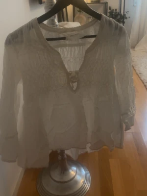 Vit Odd Molly blus med broderi - Söt vit blus från Odd Molly med broderade detaljer och smockad överdel. Blusen har en dekorativ rosett framtill och diskreta prickar i tyget. Långärmad modell med avslappnad passform och rundad halsringning.Använt 1 gång 