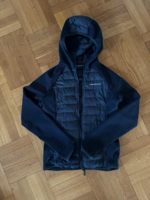 Mörkblå vindjacka från Peak Performance - Snygg mörkblå vindjacka från Peak Performance med huva och dragkedjan är tvärr najs att ha när de blåser