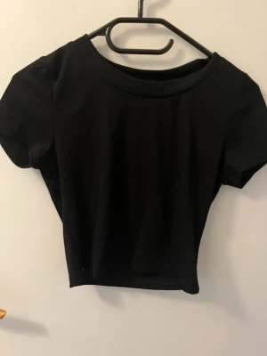 Svart croppad topp från SHEIN - En enkel och stilren svart croppad topp från SHEIN. Toppen har rund halsringning och korta ärmar. 