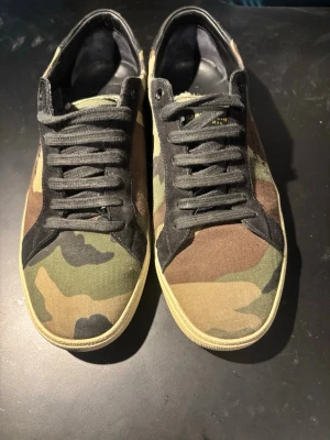 Saint Laurent camo sneakers - Säljer ett par otroligt snygga begagnade och bekväma saint Laurent skor (camo) i storleken 41 passar större. | skorna är använda och texten inuti på sulan har försvunnit samt kommer utan box skick 8/10 