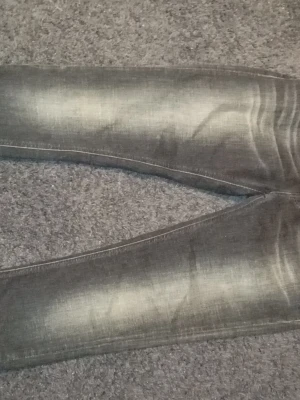 Grå slitna jeans från Nudie Jeans - Säljer ett par gråa jeans från Nudie Jeans med snygga slitningar och tvättade detaljer. Jeansen har smal passform och klassisk femficksdesign. Tillverkade i mjukt denimtyg som ger en skön känsla och cool look.
