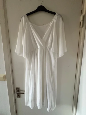 Vit omlottklänning med v-ringning - Säljer en vit omlottklänning med v-ringning och vida, korta ärmar. Glitter diamenter på. Klänningen har en luftig passform och är knälång, perfekt för varma dagar. Tillverkad i ett lätt och mjukt material som ger en skön känsla.
