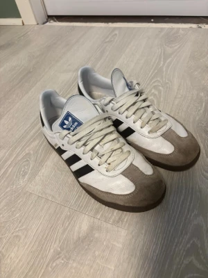 Adidas Samba  - Klassiska Adidas Samba sneakers i vitt, med bruna mockadetaljer och gummisula. Inga defekter bara lite smutsiga. 