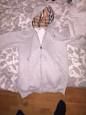 Grå zip hoodie med Burberry-mönster - Snygg grå zip hoodie från Burberry, använd 1 gång och passade inte mig i längden. Den är i storlek M men skulle säga att den känns mer som S.
