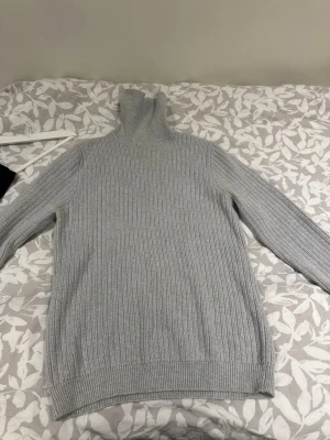 Ljusgrå polotröja These Glory Days - Säljer en ljusgrå stickad polotröja från These Glory Days. Tröjan har ribbstickad struktur, hög polokrage och långa ärmar. Perfekt för dig som gillar stilrena och klassiska plagg med en modern touch.
