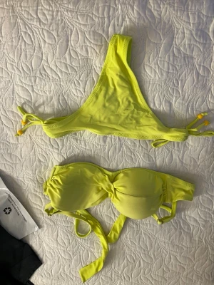 Gul bikini med knyt och bandeau - Snygg gul bikini med två olika överdelar – en trekantsmodell med knyt i sidorna och en bandeau med twist framtill och knyt i ryggen. Perfekt för soliga dagar på stranden eller vid poolen.