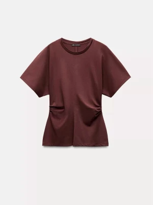 Vinröd t-shirt från Zara - Snygg vinröd t-shirt från Zara med korta ärmar och rund halsringning. T-shirten har en loose passform och coola detaljer med rynkade partier vid midjan. Perfekt till jeans eller kjol för en avslappnad look.