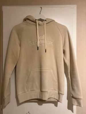 Peak Performance hoodie - Snygg beige hoodie från Peak Performance med broderad logga och text 'Est. 1986' på bröstet. Hoodien har huva med dragsko och en stor magficka framtill. Tillverkad i mjukt material som känns skönt mot huden. Perfekt för en avslappnad och trendig stil.