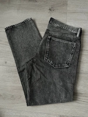 Grå tvättade raka jeans från HM - Säljer ett par grå tvättade jeans med rak passform och klassisk femficksdesign. Jeansen har en snygg vintagekänsla och är tillverkade i ett robust denimtyg. Perfekta för en avslappnad och trendig look.