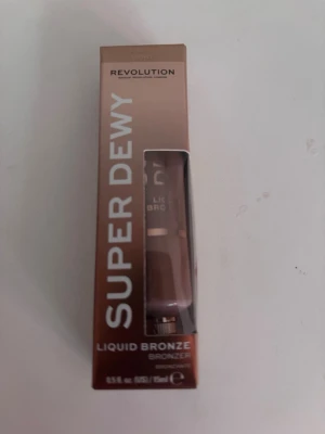 Revolution Super Dewy Liquid Bronze - Flytande bronzer från Revolution i nyansen Super Dewy. Kommer i en brun tub med transparent fönster på förpackningen. Ger en fräsch, solkysst look och är enkel att applicera för naturlig lyster. Innehåller 15 ml.