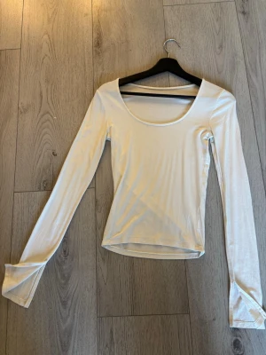 Vit långärmad topp med rund hals - En enkel och stilren vit långärmad topp med rundad halsringning och snittade ärmar. Tillverkad i mjuk bomull som känns skön mot huden. Perfekt att matcha med jeans eller kjol för en clean look.