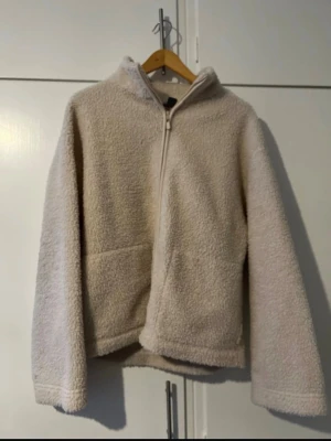 Beige teddyjacka med huva - Mysig beige teddyjacka med dragkedja framtill och huva. Jackan har två sidofickor och är tillverkad i ett fluffigt, mjukt material som håller dig varm. Perfekt för kyliga dagar och enkel att matcha med olika outfits.Pris kan diskuteras 