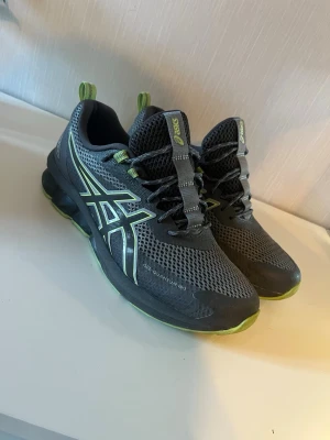 ASICS Gel-Quantum 180 sneakers - Snygga ASICS Gel-Quantum 180 sneakers i svart och grå mesh med limegröna detaljer. Skorna har en sportig design med synlig gel-sula och reflekterande logga på sidan. Perfekta för dig som gillar streetwear och komfort. Klassisk snörning och ventilerande material.