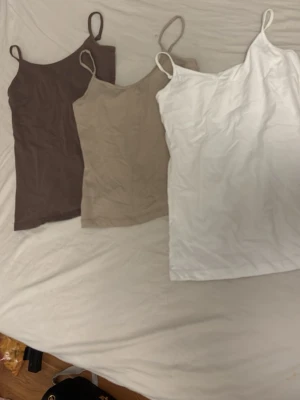 3-pack linnetoppar i neutrala färger - Tre stilrena linnetoppar i brunt, beige och vitt. Alla har smala axelband och rak passform, perfekta att matcha till olika outfits. Tillverkade i mjukt material som känns skönt mot huden.