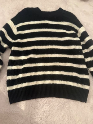 Randig svartvit stickad tröja - Stickad tröja från H&M i svart och vitt med breda ränder. Tröjan har rund halsringning, långa ärmar och ribbade muddar vid ärmslut och nederkant. Använd några gånger men inte skador på den för det!
