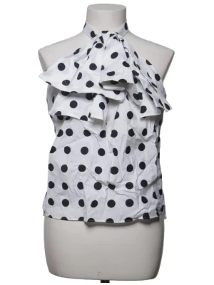Vit prickig halterneck blus med rosett - Snygg vit blus med stora svarta prickar och halterneck. Framtill finns en stor dekorativ rosett och volangdetaljer som ger extra statement. Perfekt för dig som vill sticka ut med ett lekfullt mönster och cool design.
