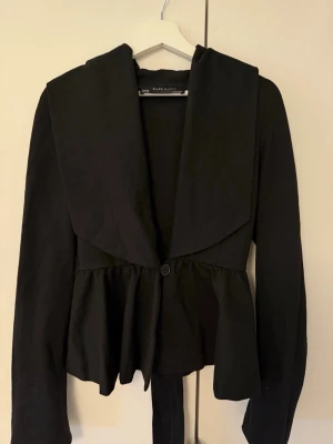 Svart kavaj - Svart kavaj/kappa med knapp framtill samt band runt från Zara, storlek M