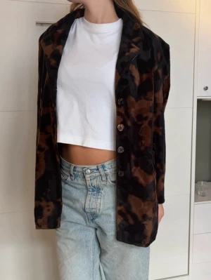 Brun och svart mönstrad kavaj - Snygg kavaj med brun och svart mönstring i sammetstyg. Rak passform med knäppning framtill och klassisk krage. Perfekt för dig som vill sticka ut med en cool och trendig look. Obs, uppskattar till storlek 40 då den ska vara oversized, men bär själv 36/38. 