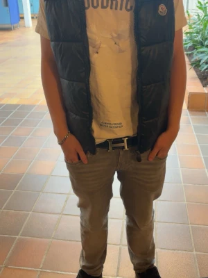 Svart dunväst från Moncler - Snygg svart dunväst från Moncler med glansig finish och klassisk logga på bröstet. Västen har dragkedja framtill och två sidofickor med dragkedja. Perfekt för lager-på-lager och streetstyle.