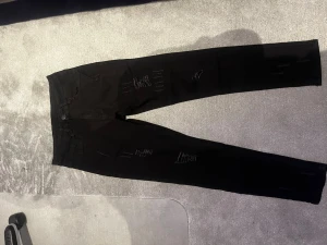 Svarta skinny jeans med slitningar - Säljer ett par svarta skinny jeans med snygga slitningar framtill. Jeansen har klassisk femficksdesign och smal passform som sitter tight längs benen. Perfekta för en trendig och avslappnad stil.