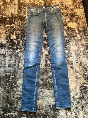 Blå skinny jeans från Replay - Snygga blå skinny jeans från Replay med klassisk femficksdesign och lätt slitna detaljer. Jeansen har låg midja och smal passform hela vägen ner. Perfekta för en trendig och avslappnad look.