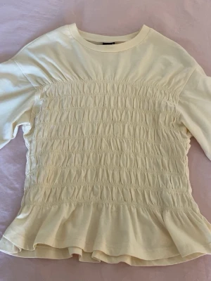 Ljusgul topp med volang från Gina Tricot💓 - En ljusgul topp från Gina Tricot med smockad framsida och volang nertill. Toppen har rund halsringning och korta ärmar. I storlek s💓