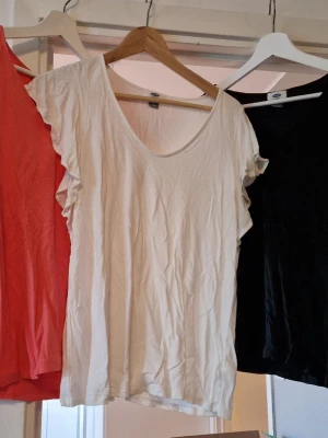 3 volangärmade toppar från Old Navy - Säljer 3 toppar från Old Navy i storlek M i färgerna vit, svart och korall. Topparna har volangdetaljer längs ärmarna och en djup v-ringning. Tillverkad i tunn, mjuk viskos som faller fint. Perfekt för varma sommardagar när man vill känna sig lite mer klädd men ändå sval och bekväm. 
