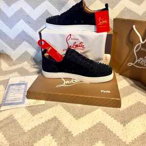 Christian Louboutin marinblå sneakers - Marinblå sneakers från Christian Louboutin med ikoniska röda sulor och blå nitar på tån. Skorna har en låg silhuett, snörning och är tillverkade i mocka. Perfekt för dig som vill sticka ut med exklusiv design och detaljer.
