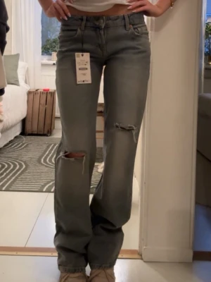 Raka jeans med slitningar - Snygga grå/blå jeans med raka ben och slitningar på båda knäna och vid ena ankeln. Använda några få gånger så inga prislappar kvar.
