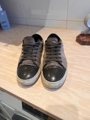 Grå mockasneakers med svart tå - Snygga sneakers i grå mocka med svart tåparti i skinn och vita sulor. Skorna har svarta snören och en klassisk låg profil som passar till många olika stilar. Perfekta för dig som gillar en stilren och modern look.