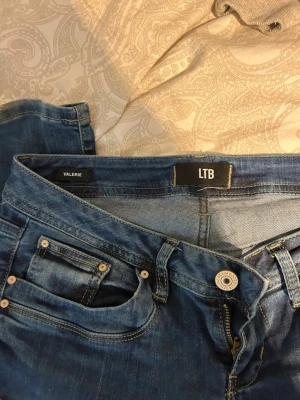 Blå jeans från LTB Valerie - Snygga blå jeans från LTB, modell Valerie. Klassisk femficksdesign med silverfärgade nitar och knapp. Storlek 27/34! Jeansen har en smal passform och är tillverkade i ett stretchigt denimtyg för extra komfort.