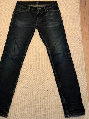 Mörkblå slim fit jeans - Snygga mörkblå slim fit jeans med klassisk femficksdesign och diskreta slitningar. Jeansen har smal passform och normal midja, med väldigt snygga fades