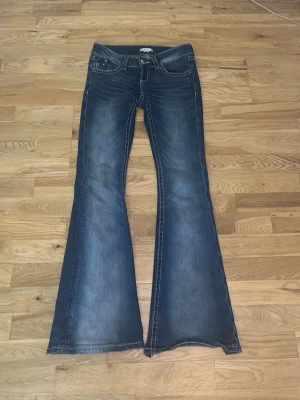 Mörkblåa jeans  - Jag säljer ett par blåa bootcut jeans från Gina tricot o storlek XS 14+. Dom är lågmidjade och är 15 cm lågmidjade, midjan är 33cm och längden är 96cm som sitter bra på mig och jag är ca 160cm lång! Vid slutet av byxorna har jag trampat sönder och klippt av en liten bit men syns knappt när man går! Byxorna är använda ganska mycket men syns knappt utom vid fötterna förstås. Fickorna har lite glitter, palieter och lite på sydd tyg! Sömmen på byxorna är vita, byxorna är lite kvarg byx aktigt! 