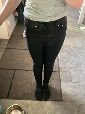 Svarta läder skinny jeans med hög midja - Säljer ett par svarta läder skinny jeans med hög midja och klassisk femficksmodell. Jeansen har en glansig finish som ger en cool look och sitter tight hela vägen ner. Perfekta till sneakers eller boots.