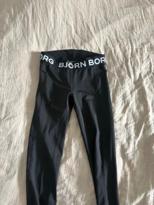 Svarta leggings från Björn Borg - Snygga svarta leggings från Björn Borg med bred resår i midjan där loggan står tryckt i vitt. Modellen är tajt och stretchig, perfekt för träning eller chill. Materialet är HYDRO-PRO som andas och känns skönt mot huden.