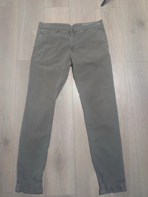 Olivgröna chinos med raka ben - Snygga olivgröna/grå chinos med klassisk passform och raka ben. Byxorna har två sidofickor fram och två bakfickor med knapp. Tillverkade i ett mjukt bomullstyg som ger en skön känsla. Perfekta för en avslappnad och stilren look.