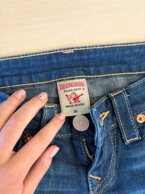 True Religion jeans modell Becky - Säljer ett par klassiska blå jeans från True Religion, modell Becky. Jeansen har tydliga kontrastsömmar, fem fickor och ikoniska läderpatches bak. Tillverkade i USA och i en snygg, tidlös blå denim. Perfekta för dig som gillar street och premium denim.